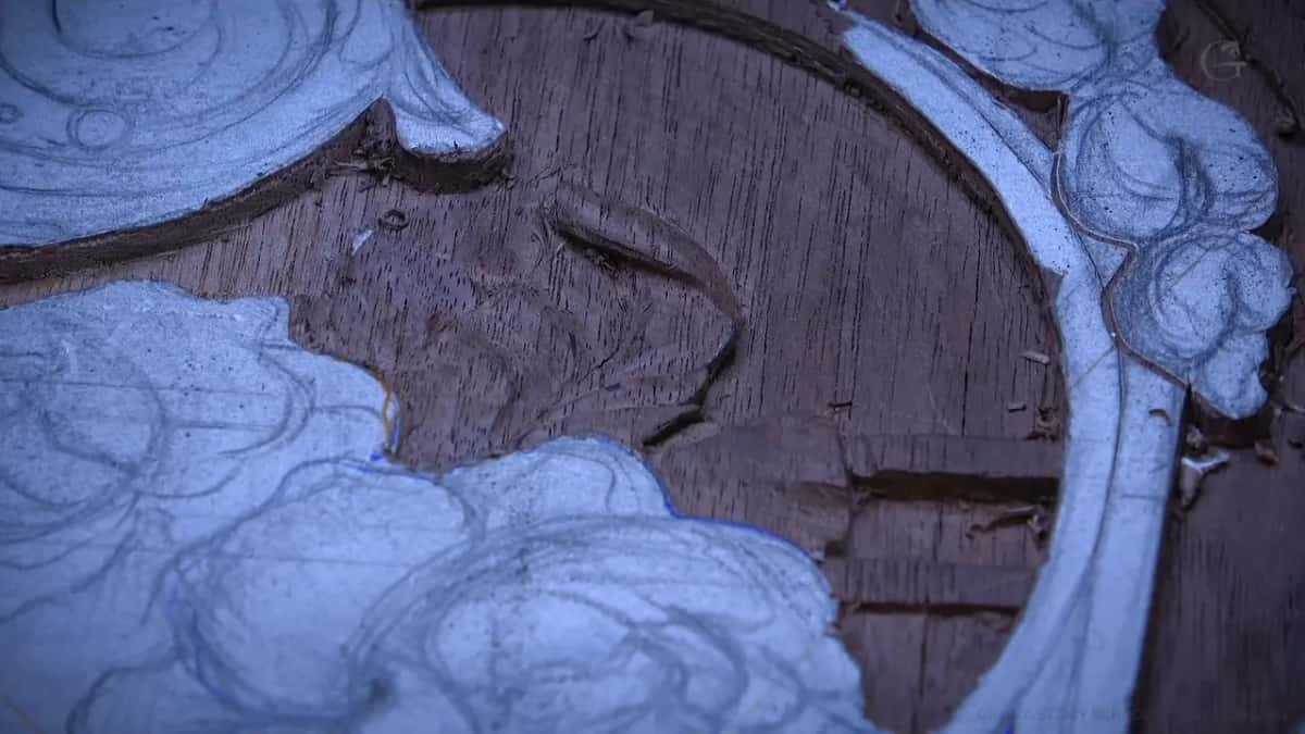 A dark open-grained panel with its raised design left pale and drawn over in pencil, background already lowered.