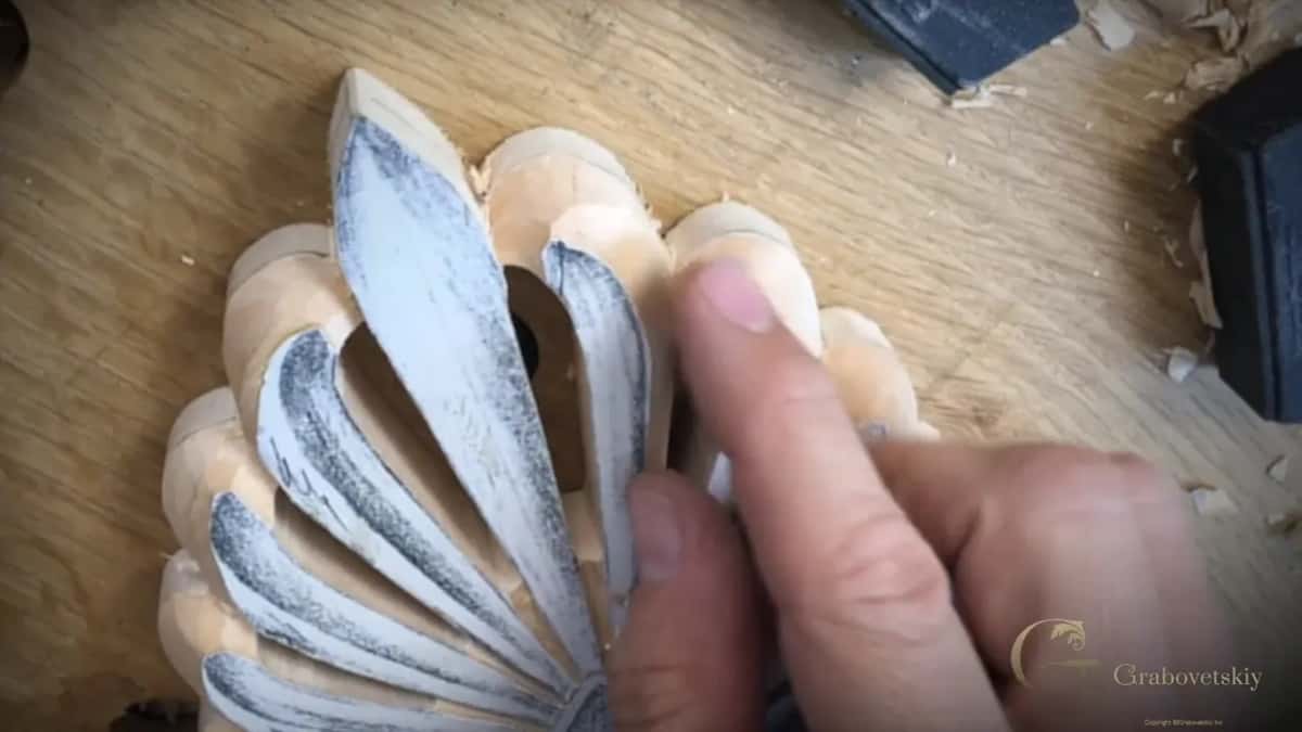 A fingertip against the outer beads of a chalked palmette where one bead has broken away.