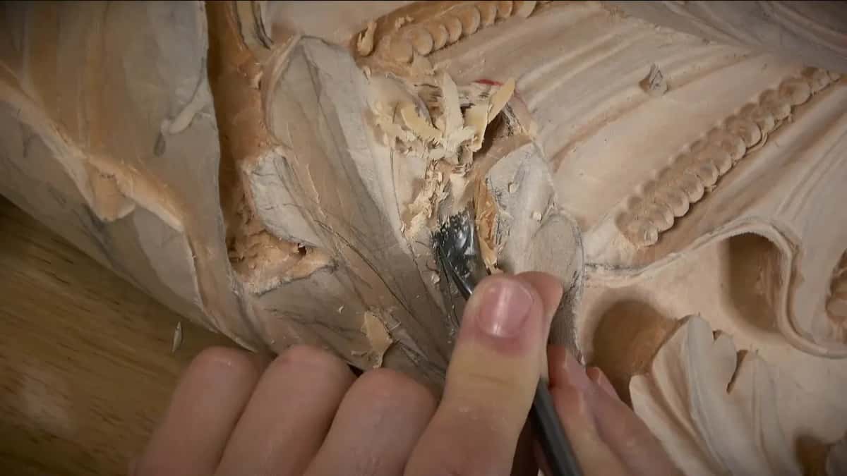 Ragged torn fibers heaped around a gouge blade in a deep carving, beaded ornament running along the right.