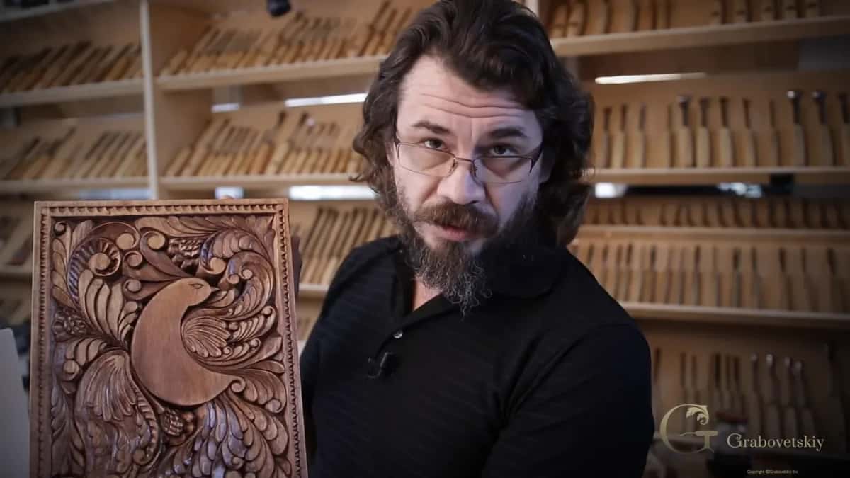 The finished bird panel, oiled Alexander Grabovetskiy holding up the finished bird panel, oiled to honey, with racks of gouges filling the wall behind him