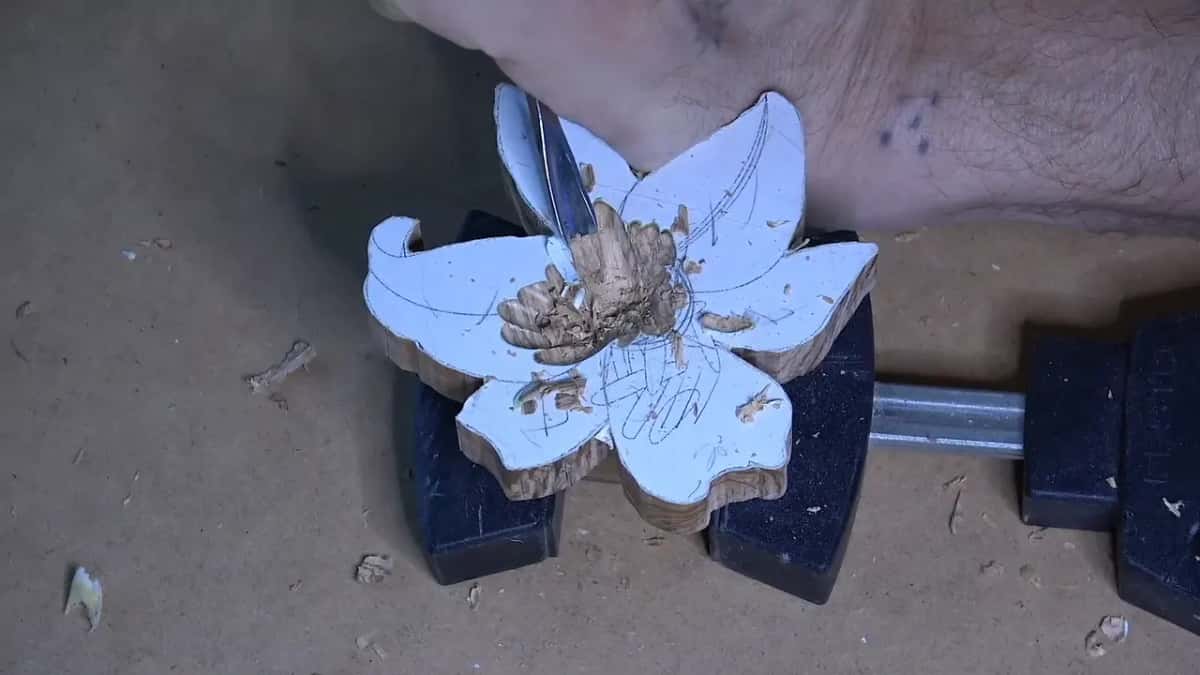 A lily blank still under its paper pattern, clamped in a vise, a gouge sinking the centre; the sawn edges show wavy figure.
