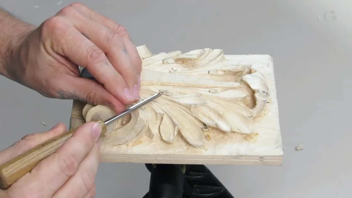 A small pale board on a ball vise with an acanthus leaf carved into it and a fine chisel resting in a deep fold.