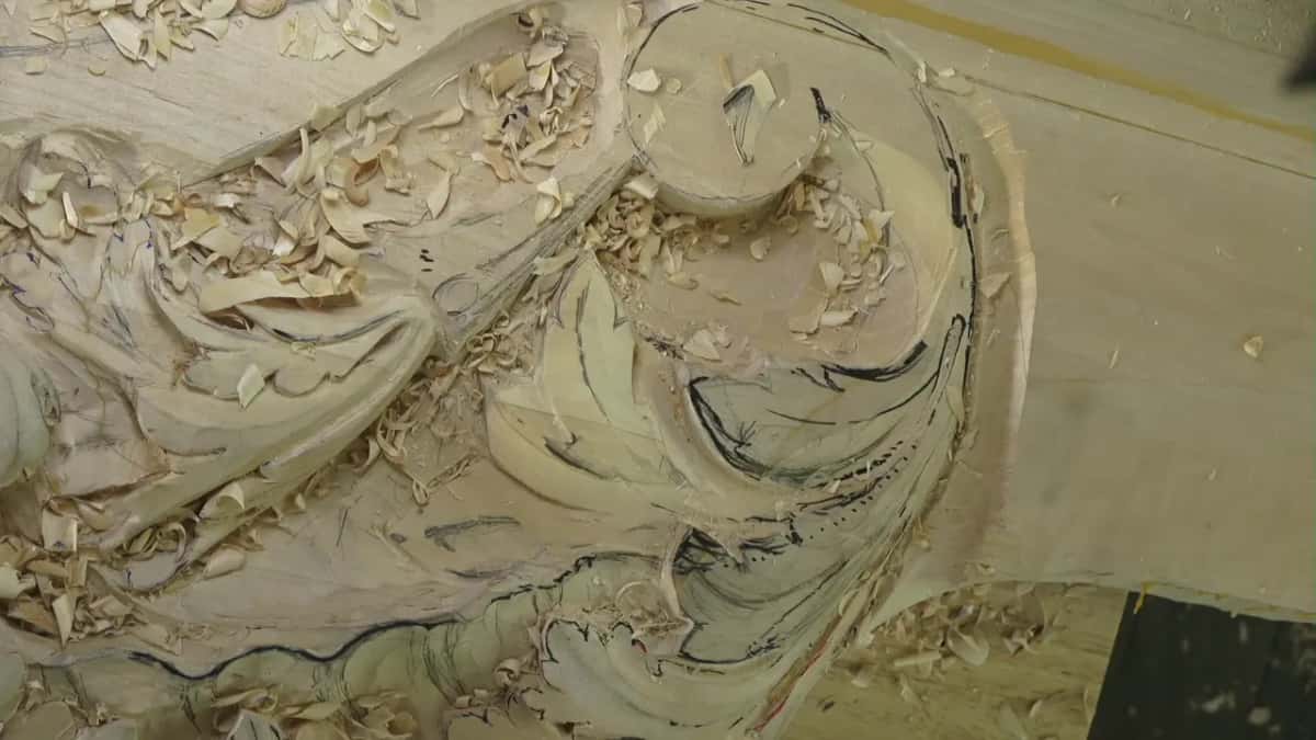 Overhead view of a pale carved panel under a heap of curled chips, marker lines still visible on the uncarved ground.